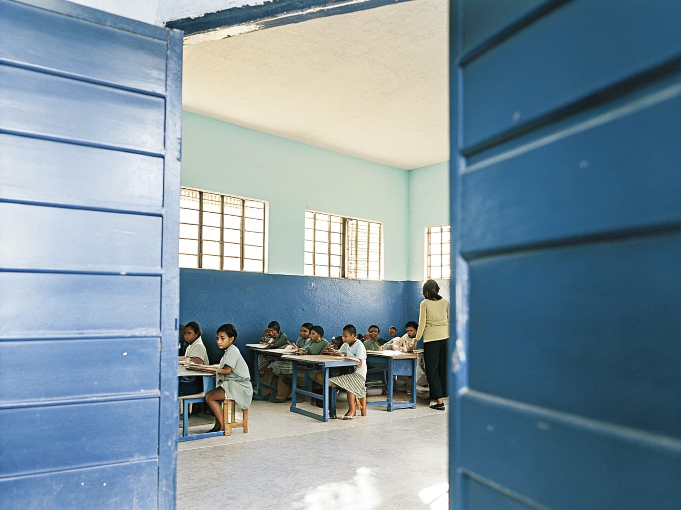 Photo of a bright elementary classroom with diverse students at desks and a teacher near a chalkboard